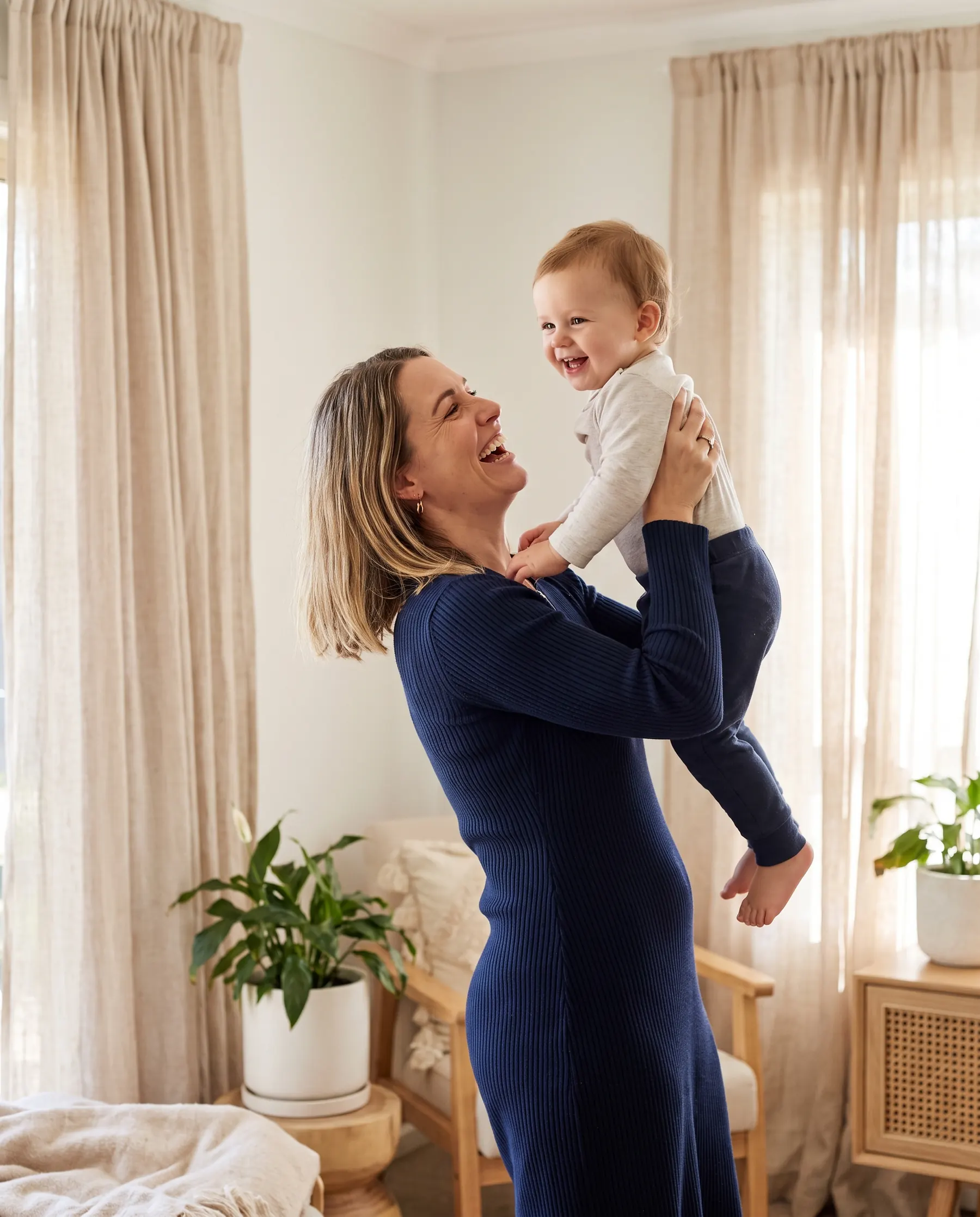 A mother laughing as she lifts her toddler at home